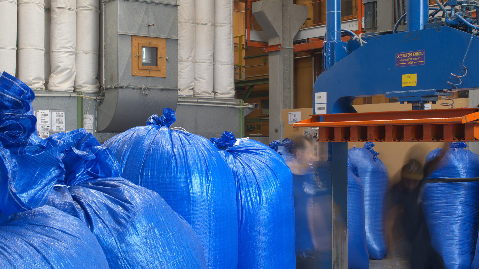 Due operatori al lavoro alla pressa, fra i big bag di piuma del reparto